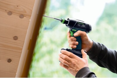 Person using a Festool cordless lithium-ion drill to fasten screws on wooden panel in home improvement setting