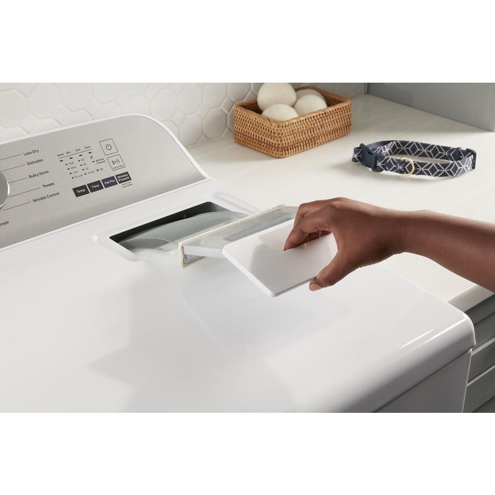 Hand opening lint trap on white top load electric dryer in modern laundry space with basket and pet collar nearby