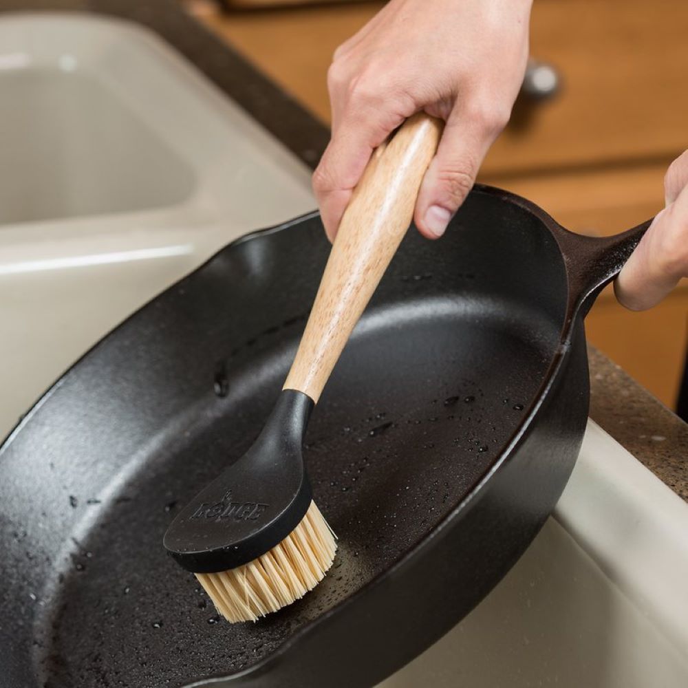 Handheld scrub brush with wooden handle and stiff nylon bristles cleaning seasoned cast iron skillet in kitchenware tools under $50 collection
