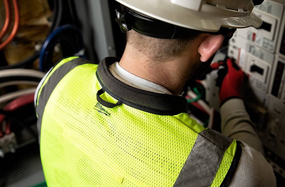 Worker wearing yellow Milwaukee high visibility mesh safety vest with reflective stripes in hardware safety gear setting