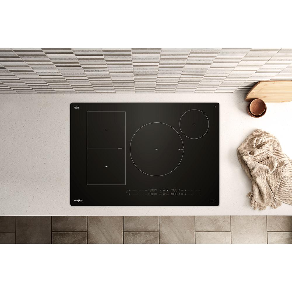 Black induction cooktop with multiple heating zones installed in white countertop with tiled backsplash and kitchen accessories nearby