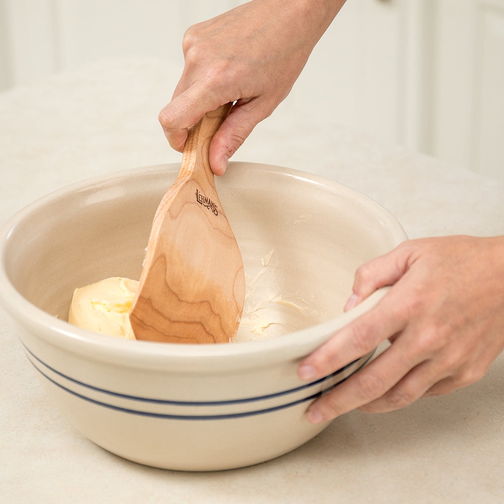 Hand using a wooden curved paddle to spread butter inside a ceramic mixing bowl for kitchenware and gadgets collections