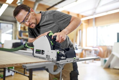 Man wearing safety glasses operating Festool plunge cut track saw with guide rail for precise home improvement cuts