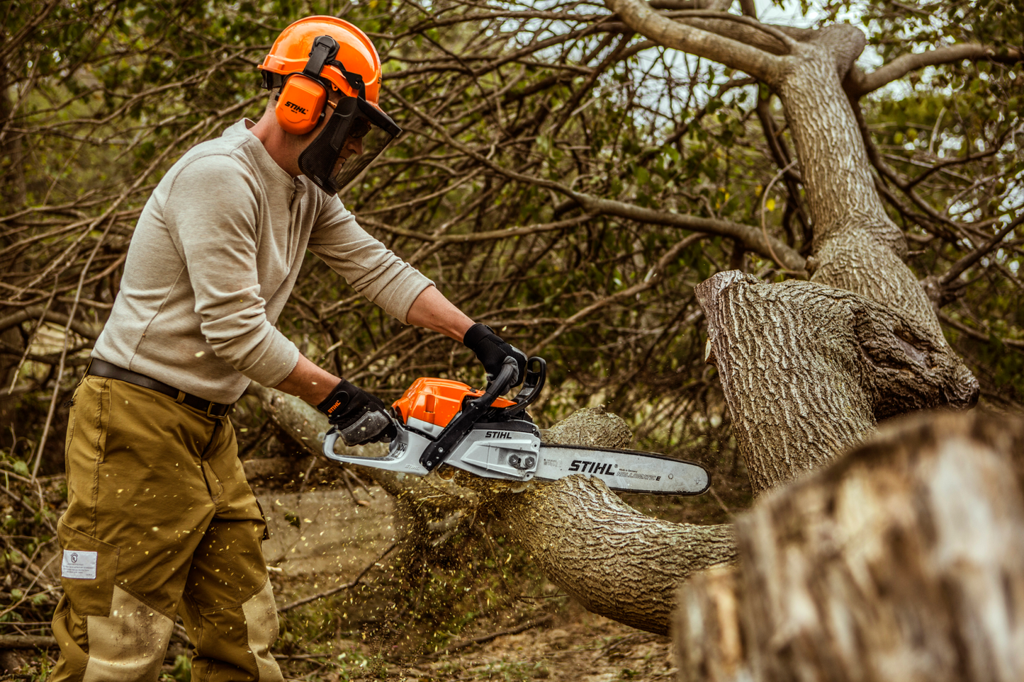 Man wearing safety gear using an 18-inch gas-powered chainsaw to cut a fallen tree in home improvement tasks