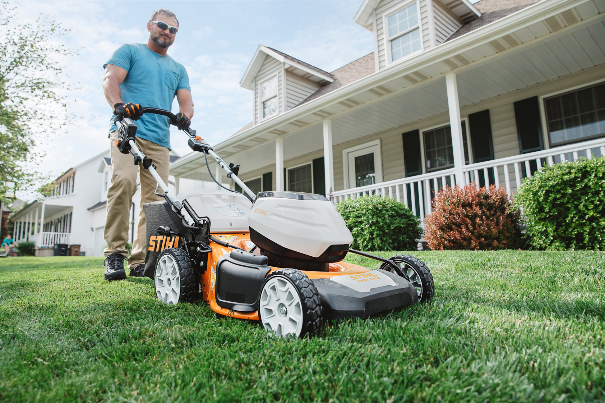 Man using a STIHL battery-powered lawn mower on a green lawn outside a suburban home in outdoor power equipment collection
