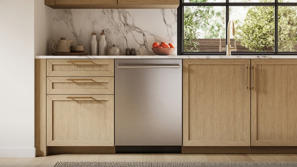 Built-in stainless steel dishwasher with anti-fingerprint finish between light wood cabinets in kitchen with marble backsplash and window view