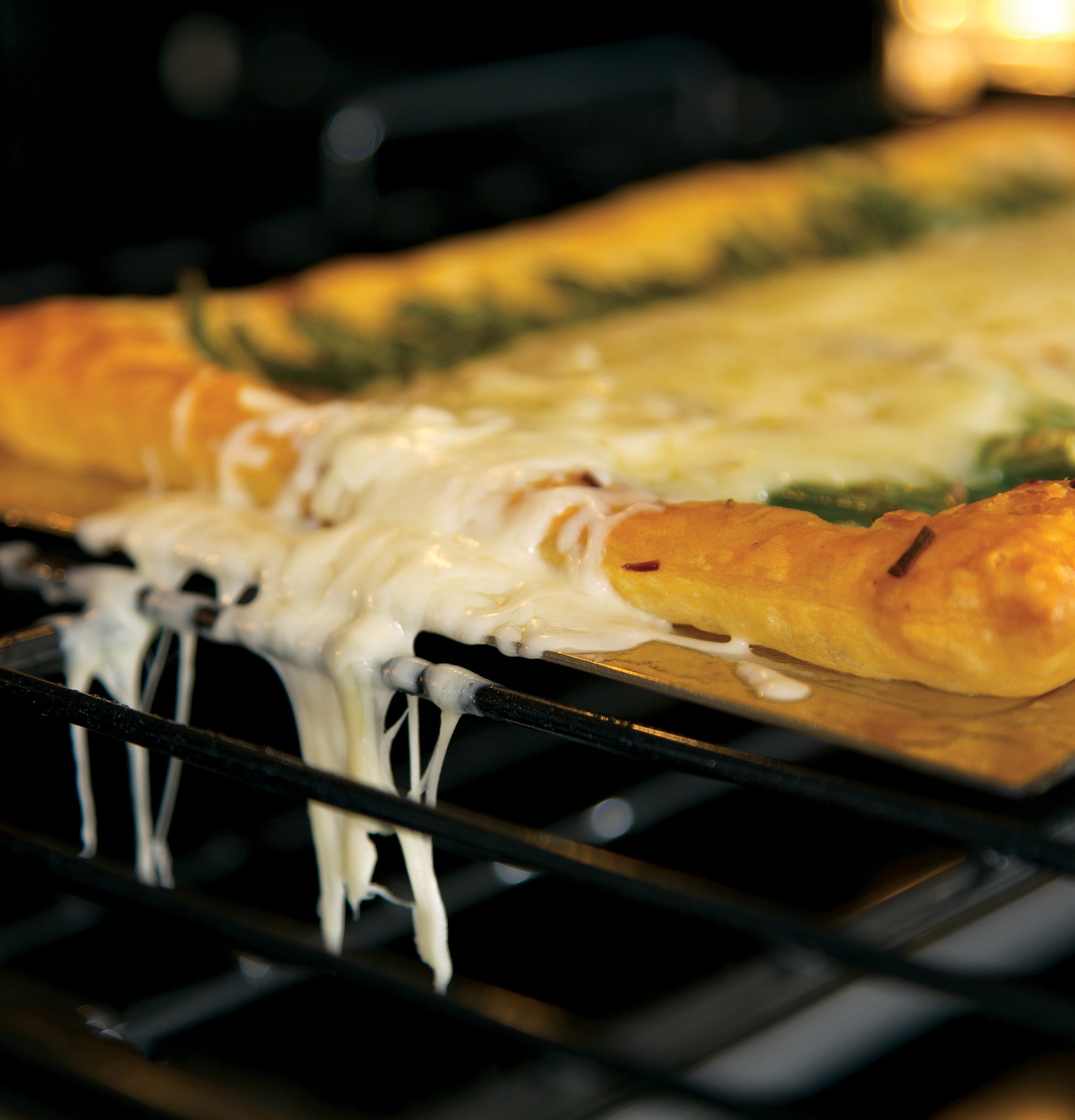 Close-up of melted cheese bubbling and dripping off a pizza baking inside a convection wall oven rack