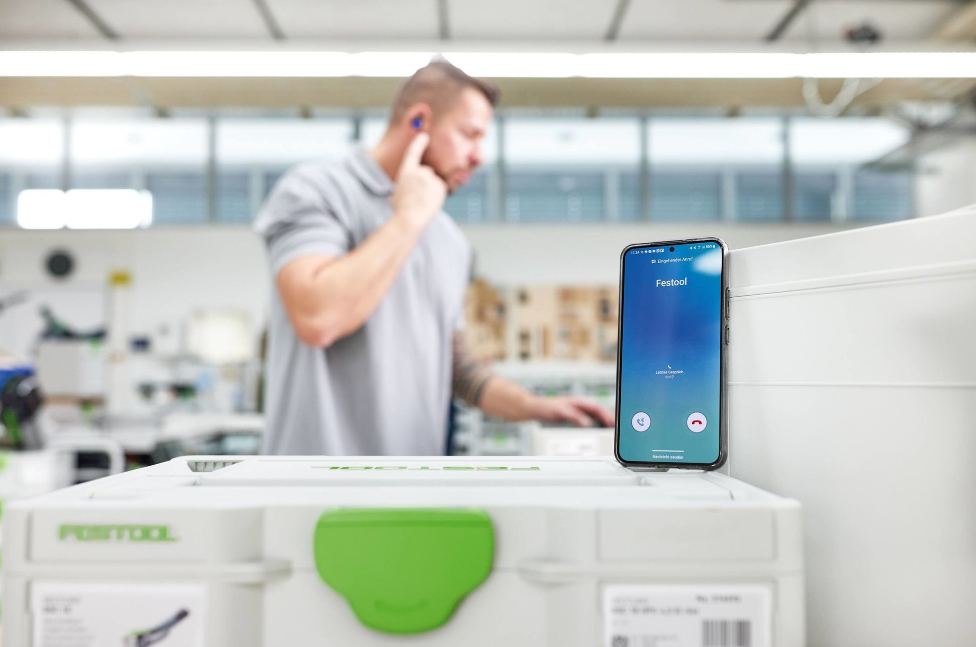 Man in workshop wearing Bluetooth earplugs while using smartphone with Festool accessories for safety and tools use