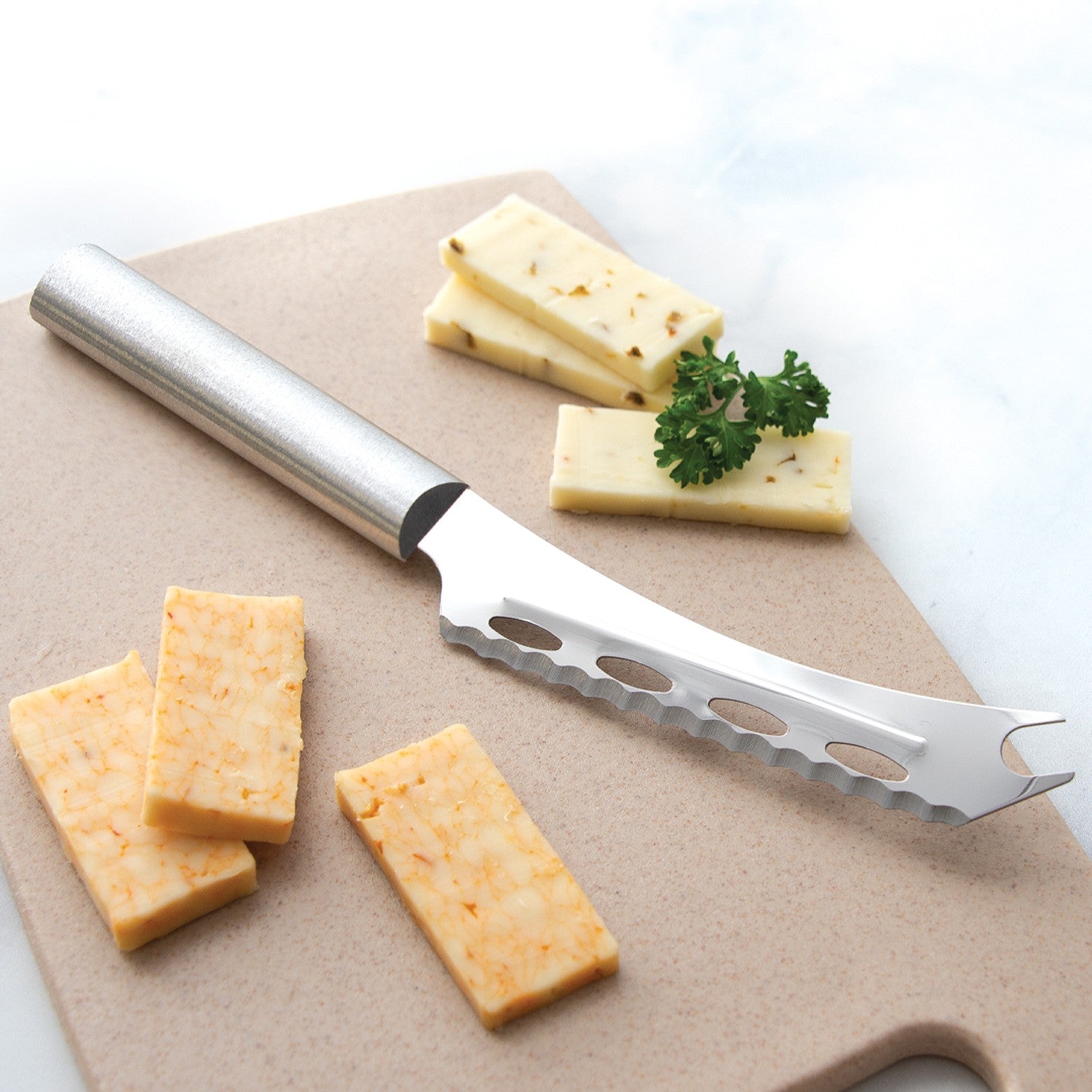 Serrated stainless steel cheese knife with holes and forked tip on cutting board with sliced flavored cheese in kitchenware