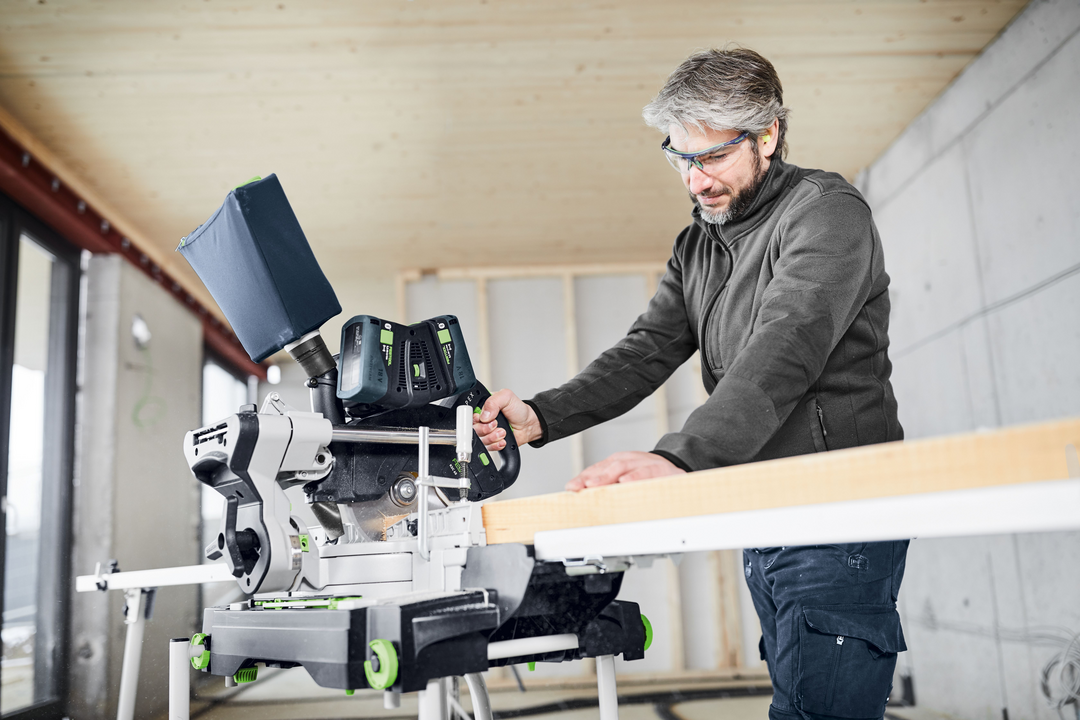 Man using Festool cordless sliding compound miter saw on wood plank in indoor home improvement workshop