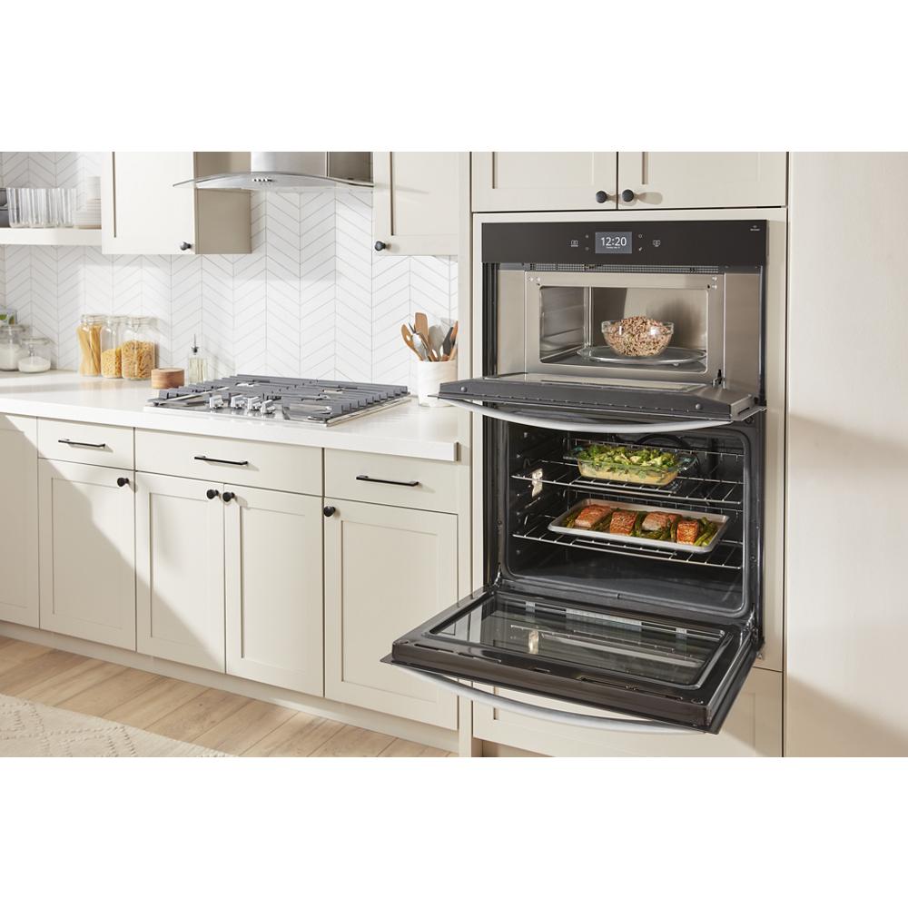 Built-in black microwave and wall oven combo with dishes inside, installed in light-colored kitchen cabinetry