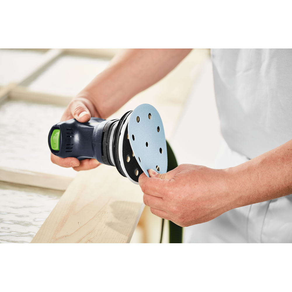 Person attaching blue sanding disc to a handheld random orbit sander for woodworking tools use