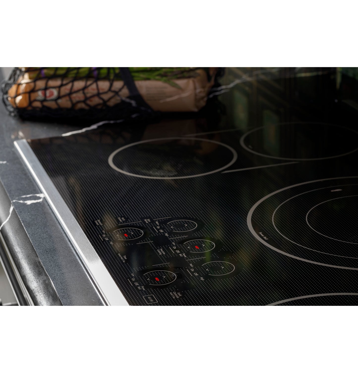 Close-up of a black touch-control electric cooktop with stainless steel trim on a dark marble countertop in a kitchen setting