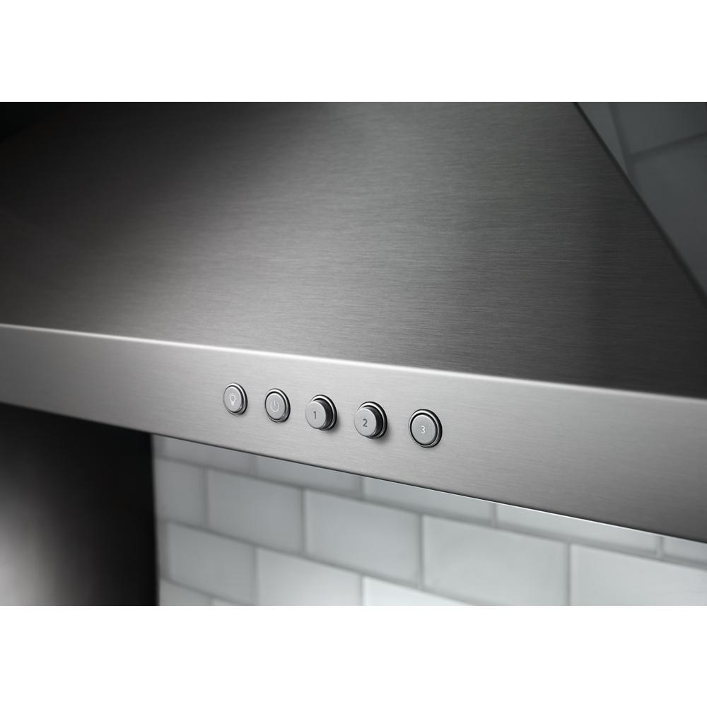 Stainless steel wall-mounted canopy hood control panel with five round buttons over white subway tile backsplash