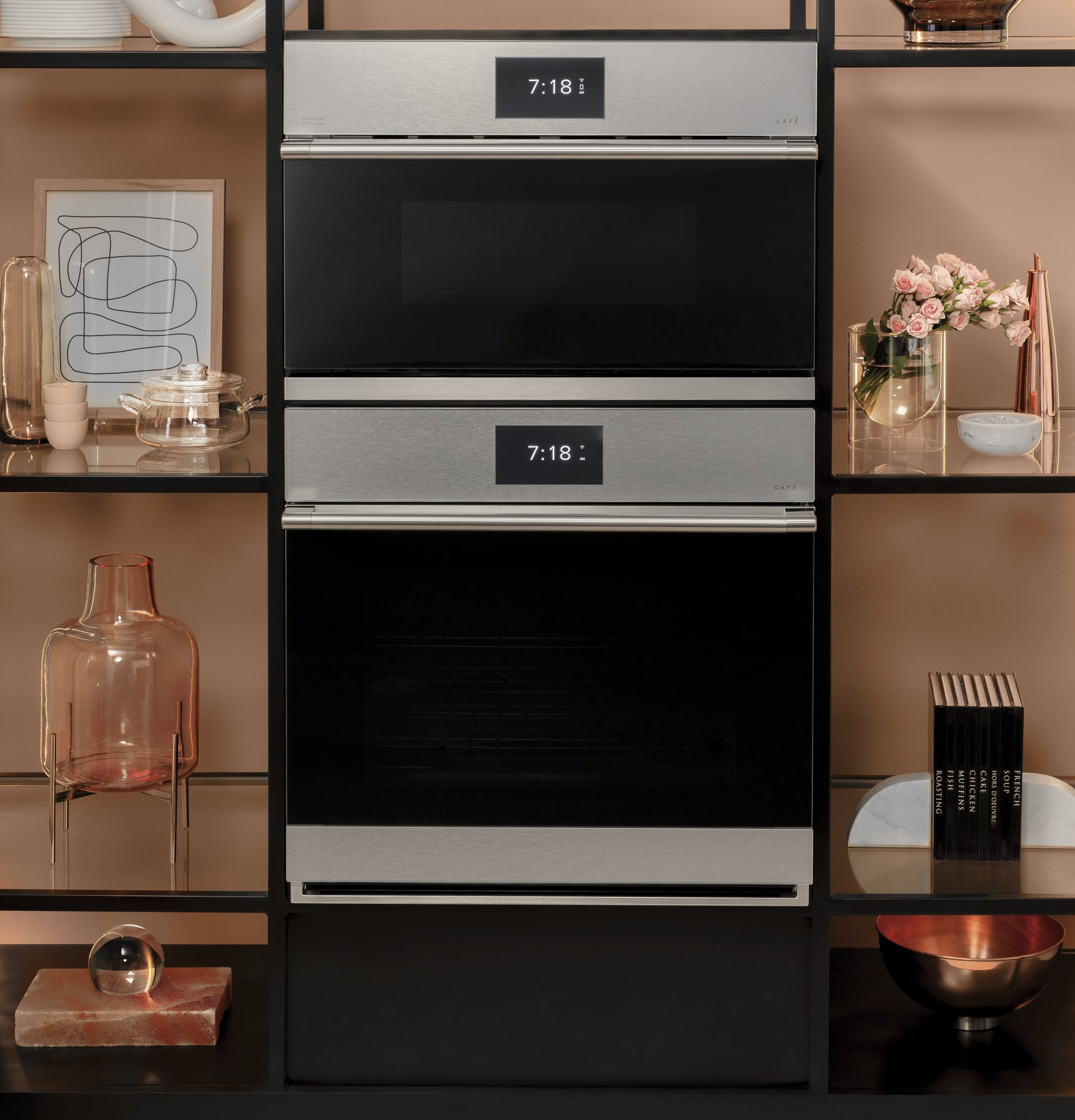 Two stacked wall ovens with platinum glass and digital clocks, styled within a modern kitchen shelving unit display