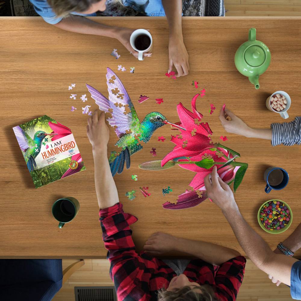 People assembling a colorful hummingbird and flower puzzle surrounded by mugs and snacks in Toys & Games collection