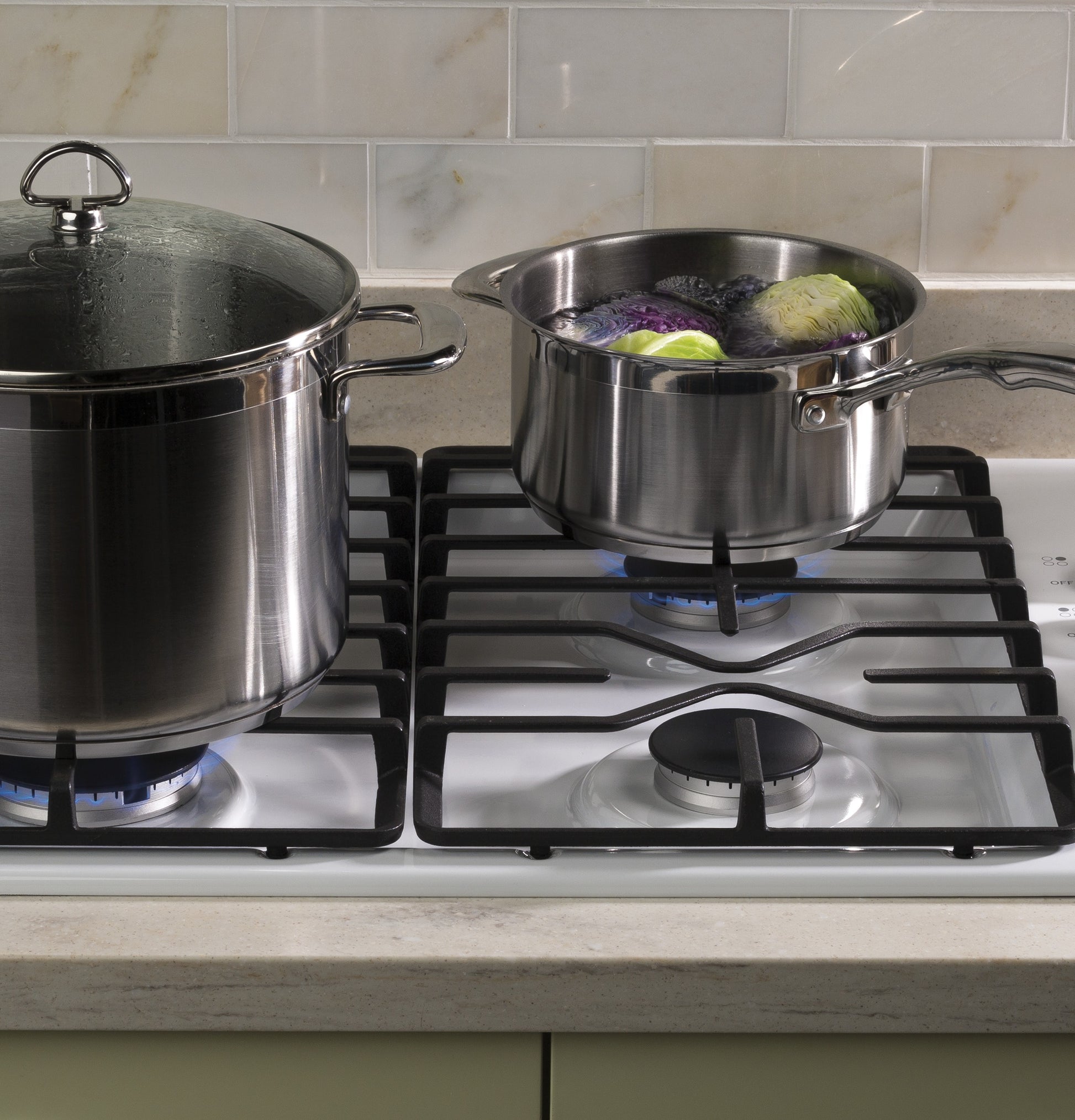 Stainless steel pots on lit burners of built-in gas cooktop in kitchen setting for home improvement use