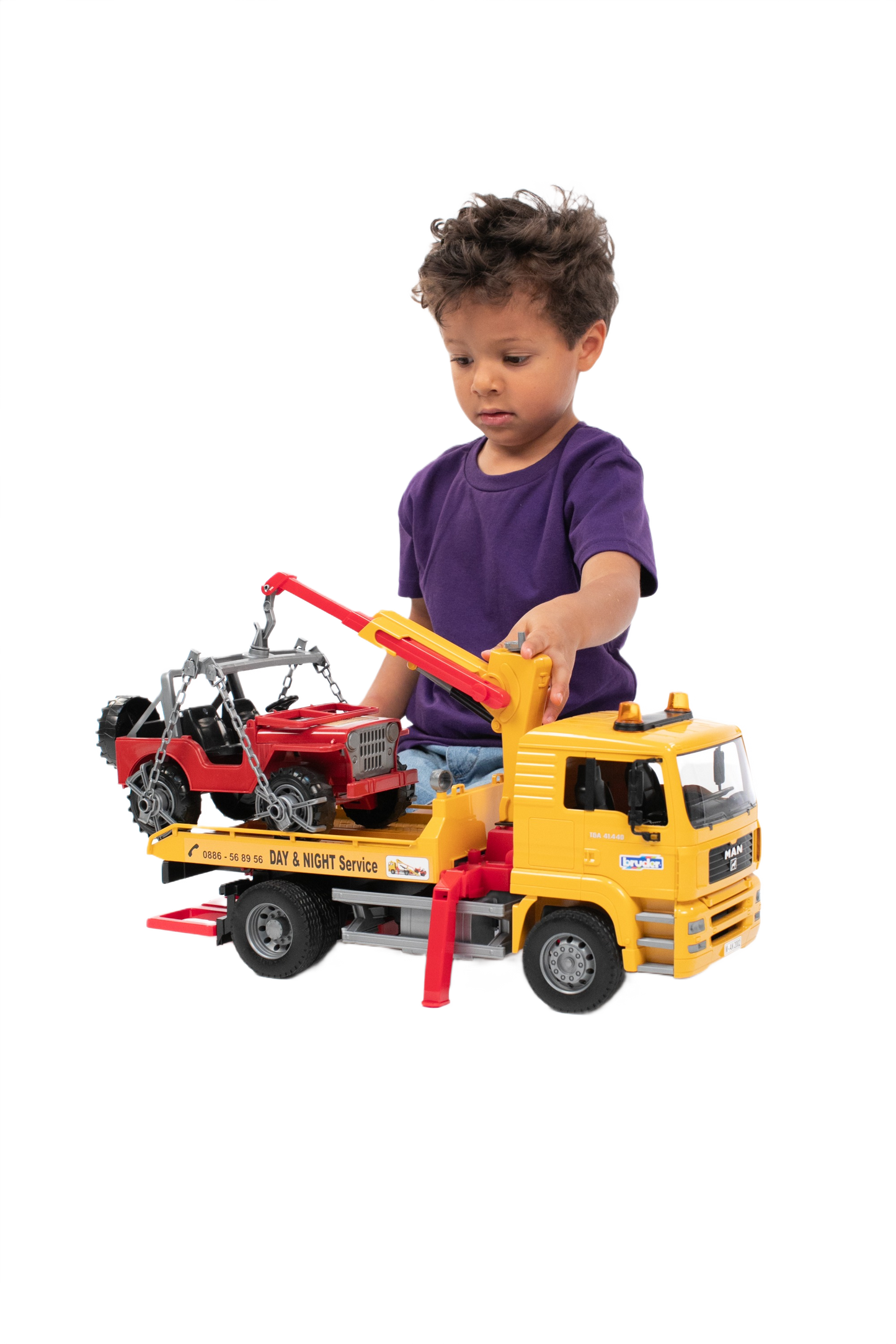 Child playing with yellow MAN TGA tow truck toy lifting red off-road vehicle on flatbed for imaginative play