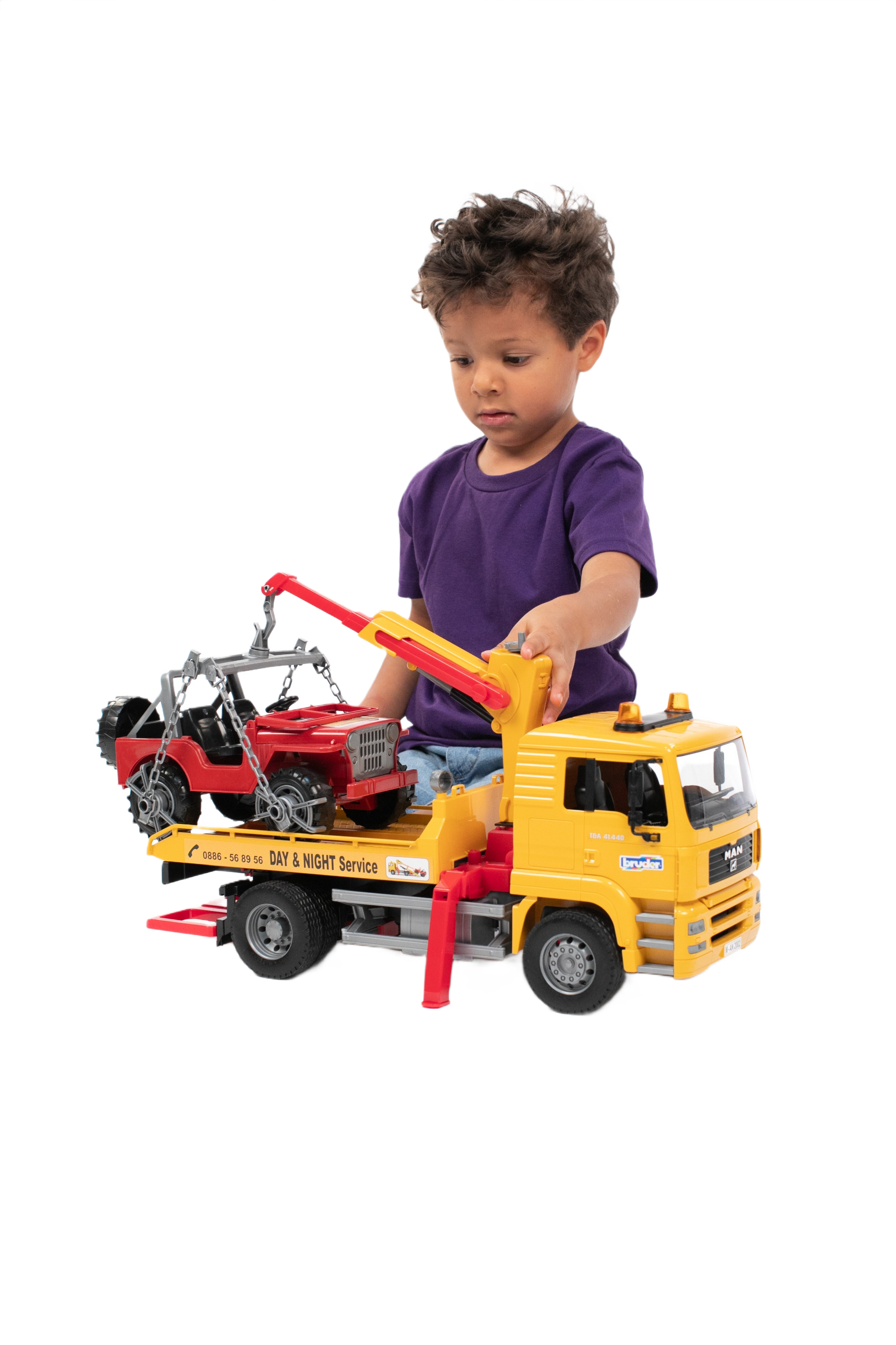 Child playing with yellow MAN TGA tow truck toy lifting red off-road vehicle on flatbed for imaginative play