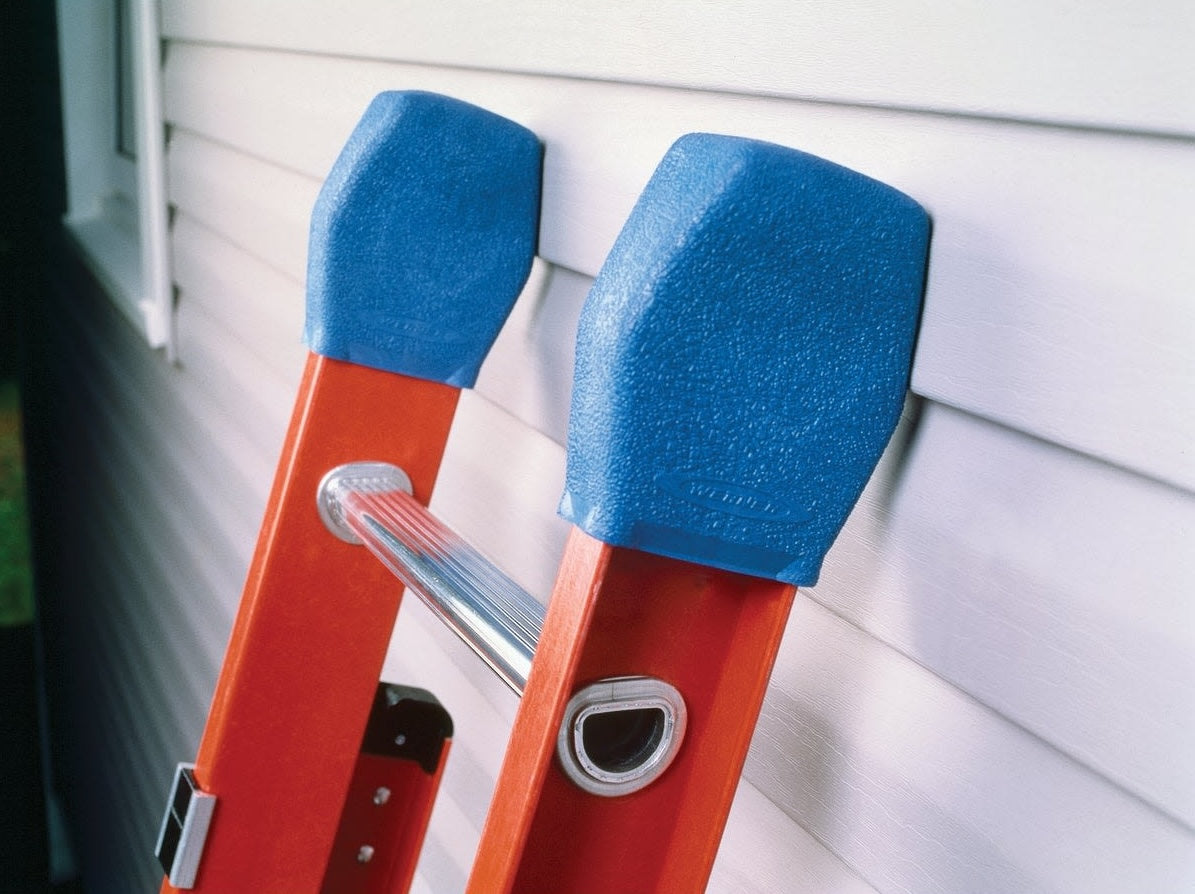 Blue protective covers fitted on top of orange ladder rails against house siding for home improvement tasks