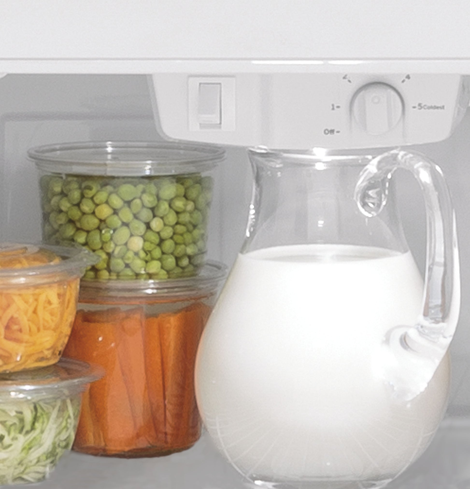 Clear containers with fresh vegetables and a glass pitcher of milk inside refrigerator interior shelves