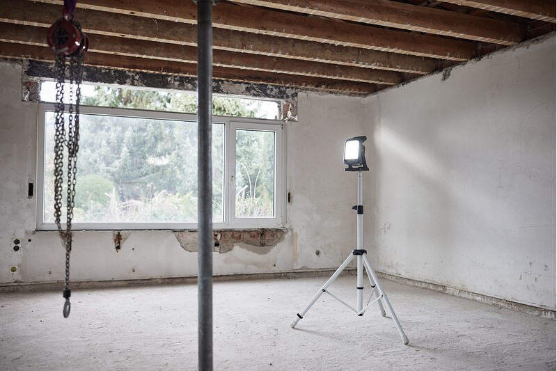 Adjustable tripod stand with locking pin supporting work light in unfinished room for tool accessories and home improvement