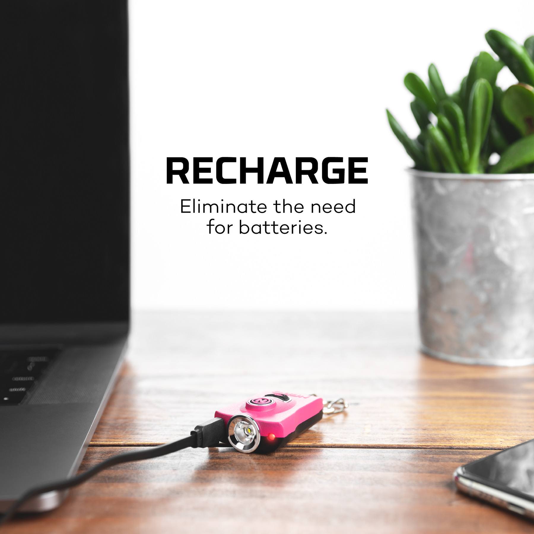 Pink rechargeable keychain light and safety alarm connected to laptop on wooden desk with plant in background
