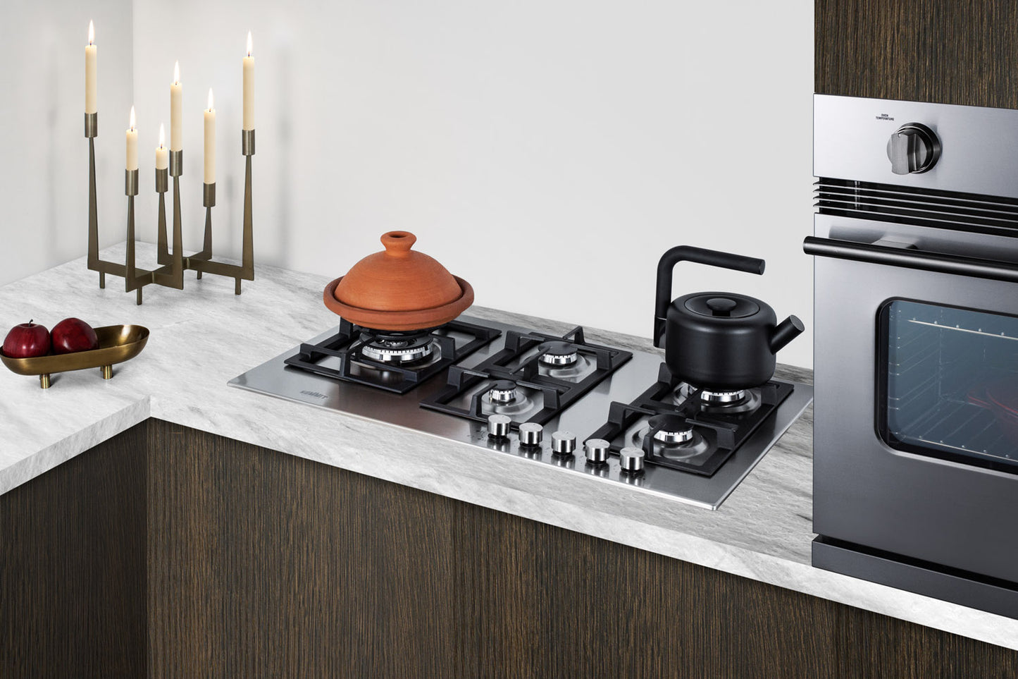 Five-burner stainless steel gas cooktop installed in modern kitchen with dark cabinetry and marble countertop