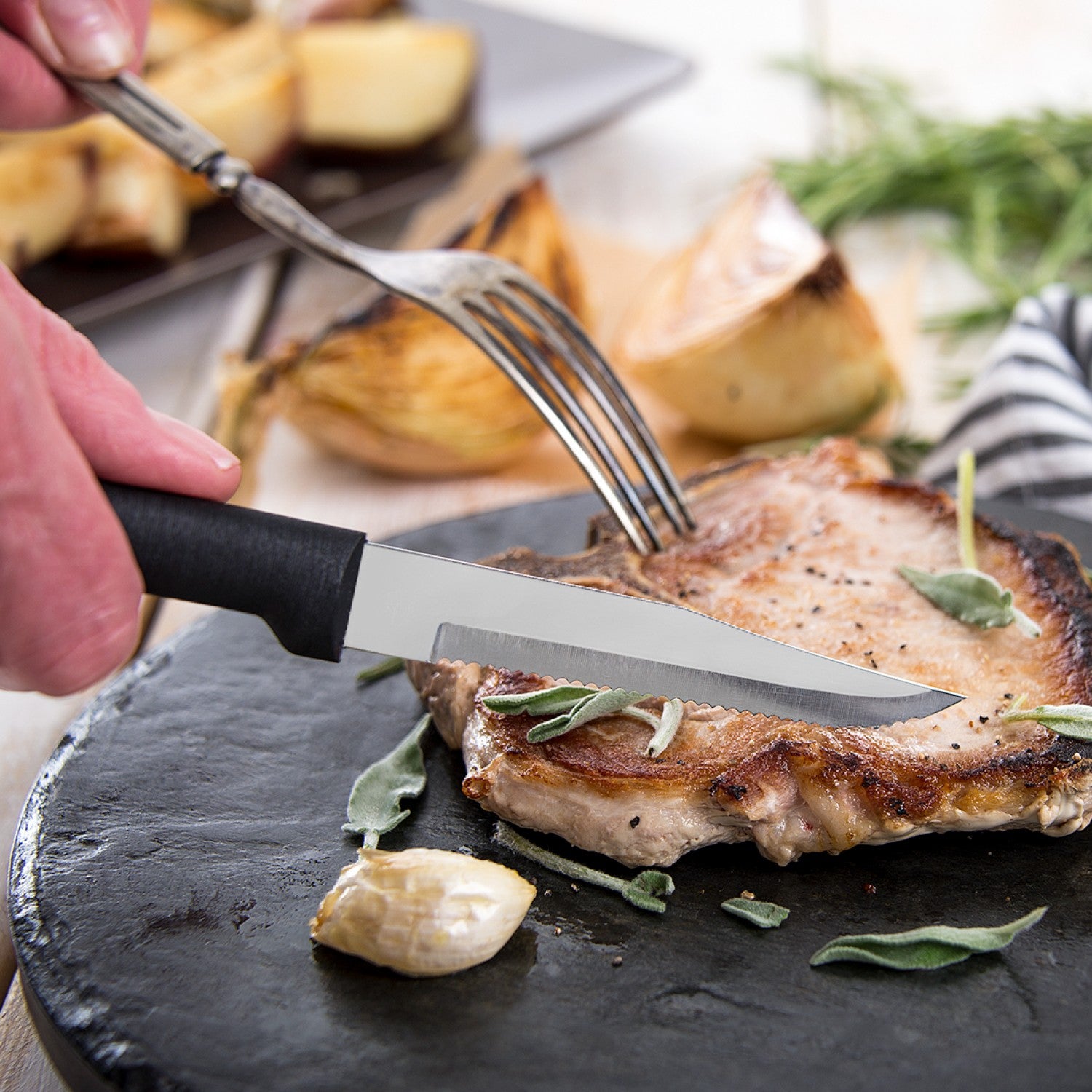 Serrated steak knife with black handle cutting cooked pork chop on black stone plate in kitchen utensils collection under $50