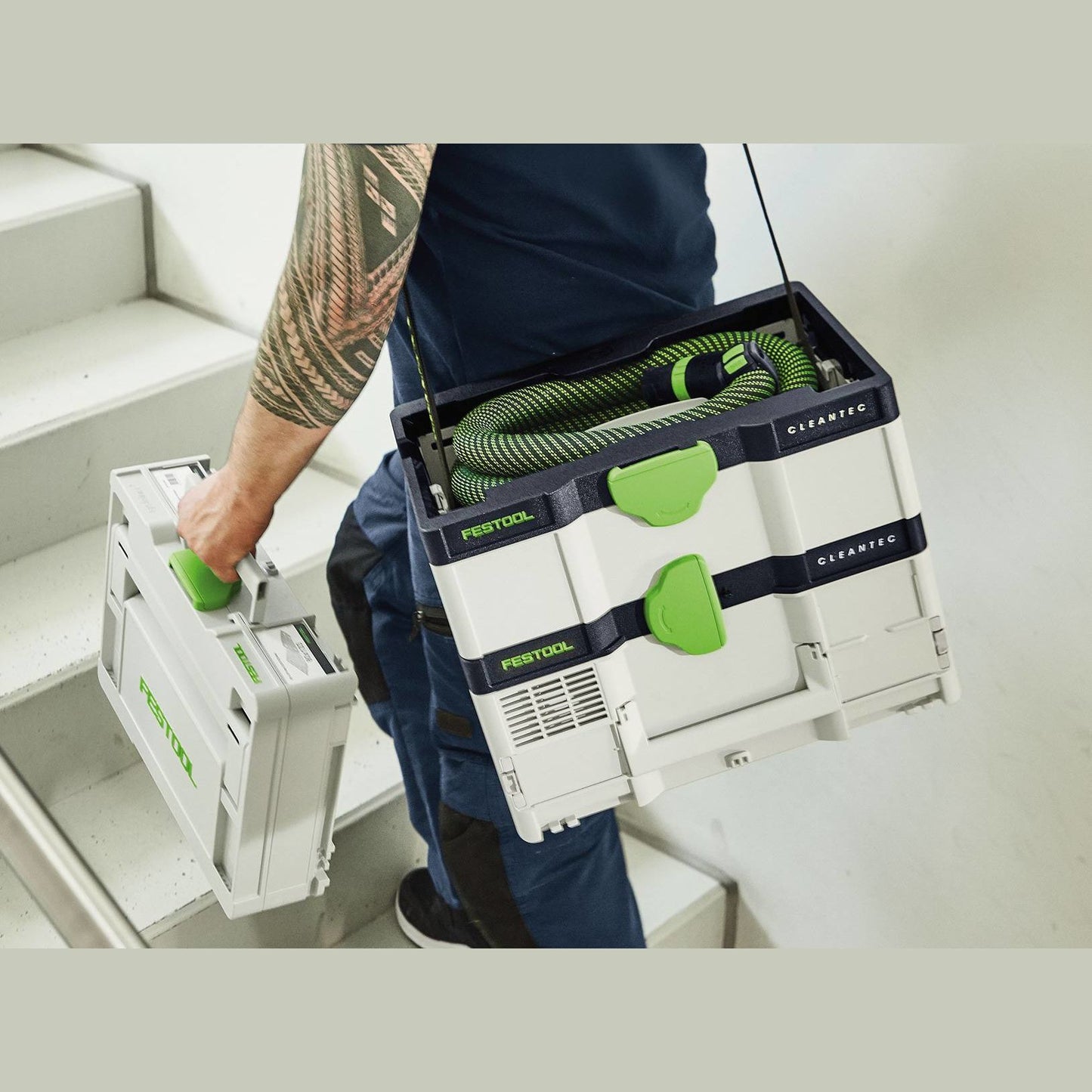 Person carrying compact Festool cordless dust extractor and storage case up stairs for woodworking tools