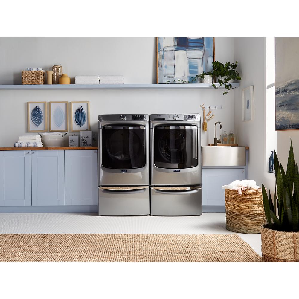 Modern laundry room with stainless steel front load washer and dryer on storage pedestals in appliance parts setting