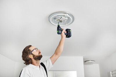 Man using Festool 576901 TXS 18-Basic cordless drill to install ceiling light fixture in home improvement task