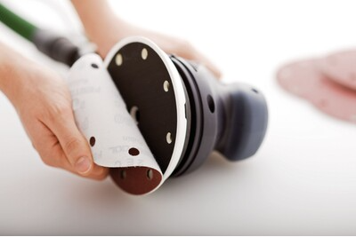 Person attaching sanding disc to Festool multi-mode sander for tools and home improvement use