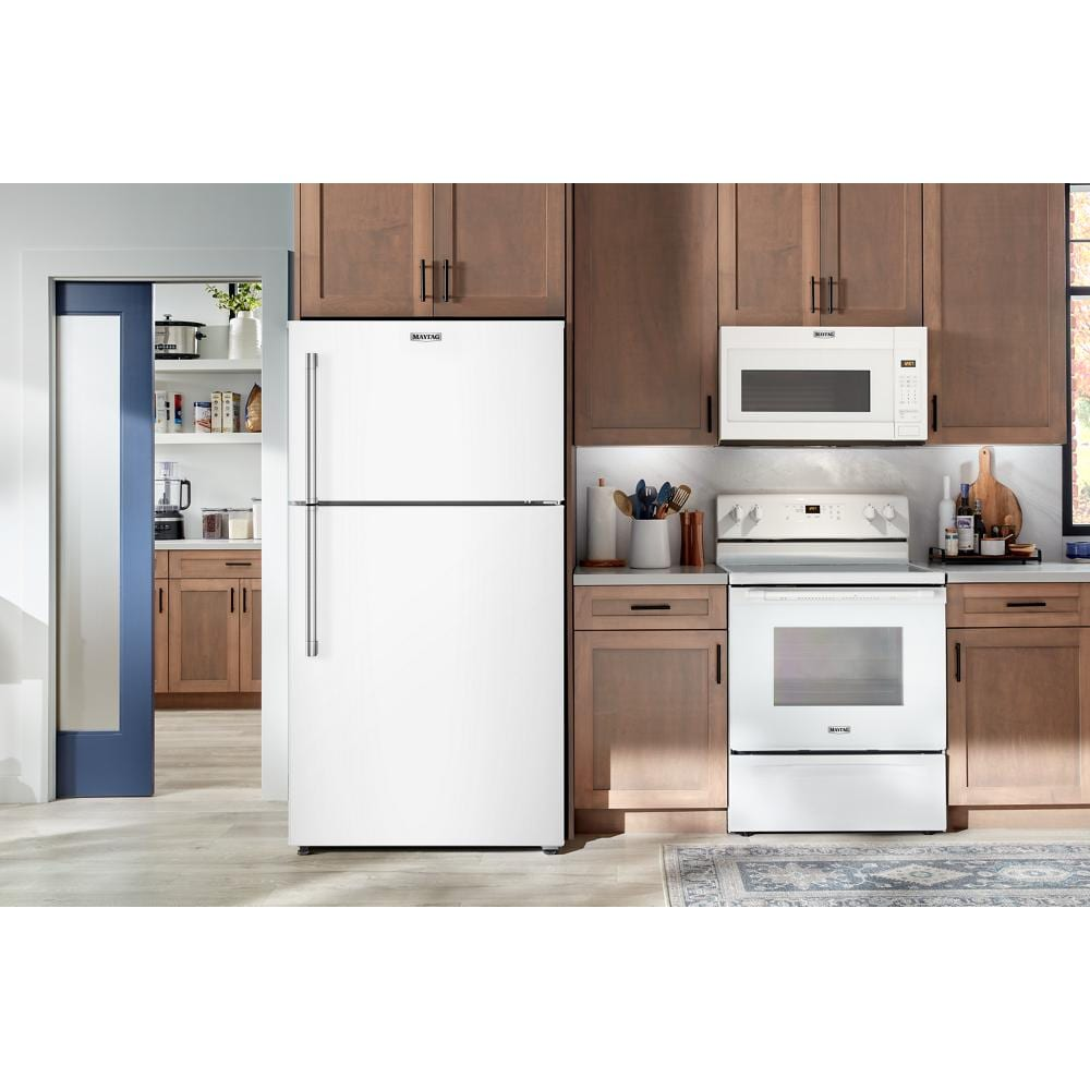 White top-freezer refrigerator with stainless steel handle in kitchen setting with wooden cabinetry and matching white appliances