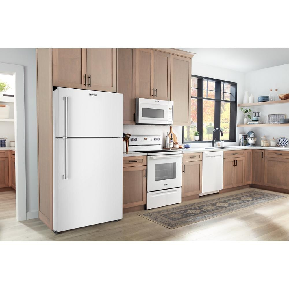 White top-freezer refrigerator installed in kitchen with wood cabinets, white appliances, and large black-framed window nearby