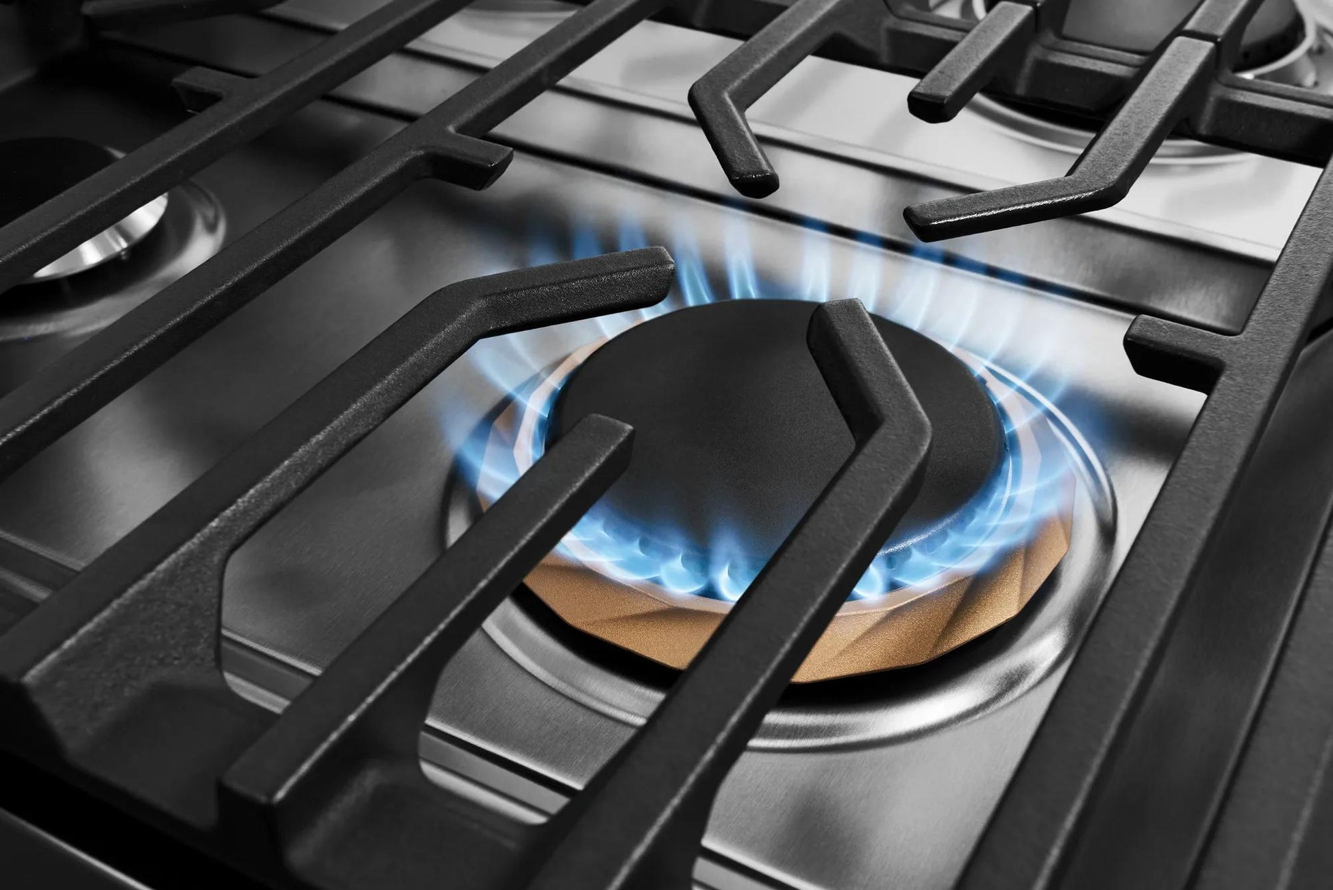 Close-up of a stainless steel gas burner ignited with blue flames in a modern kitchen range from Ranges & Cooktops collection