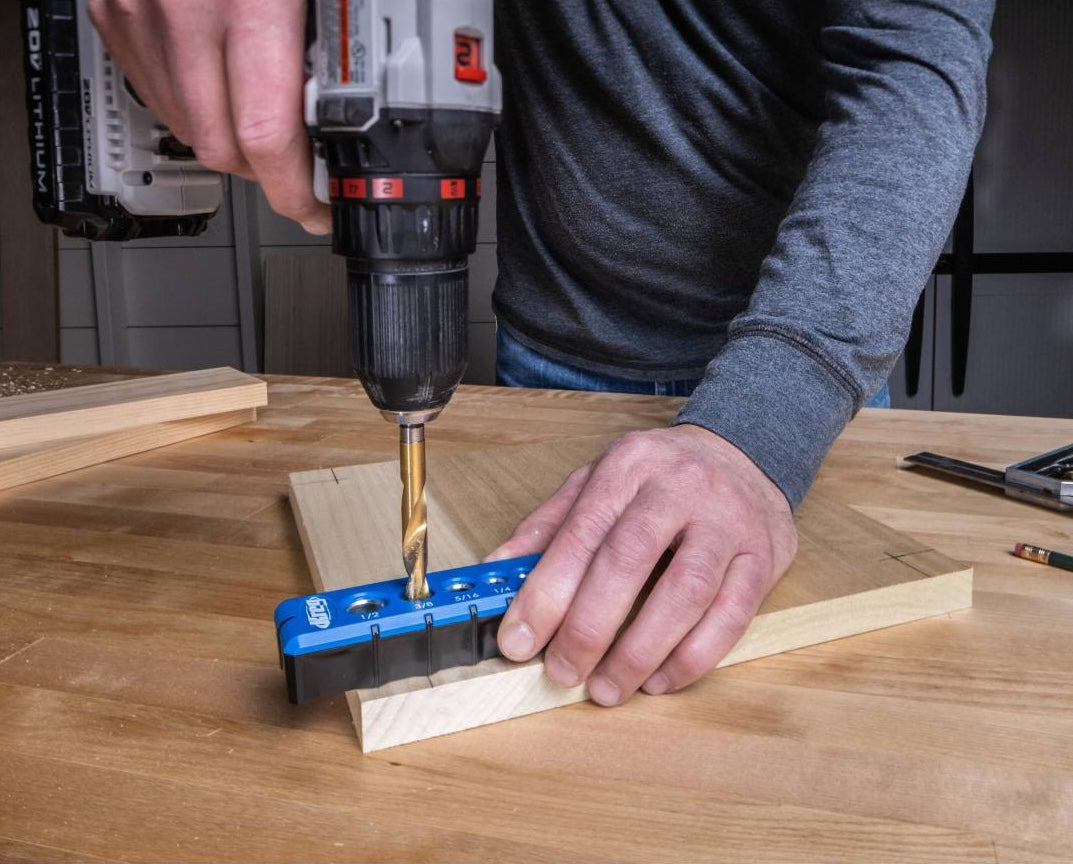 Hand using a blue drilling guide with steel drill guides to drill holes in wooden boards on a workbench in tool accessories collections