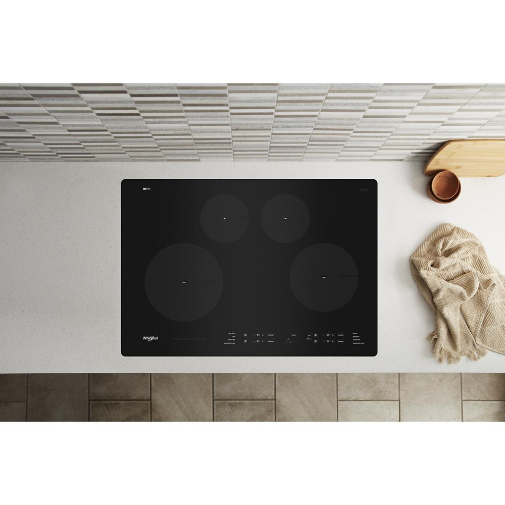 Black glass induction cooktop with four cooking zones and touch control panel on white kitchen countertop surface