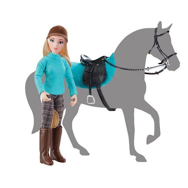 Fashion doll wearing equestrian outfit with brown riding boots and blue quilted top standing next to saddle on gray horse silhouette