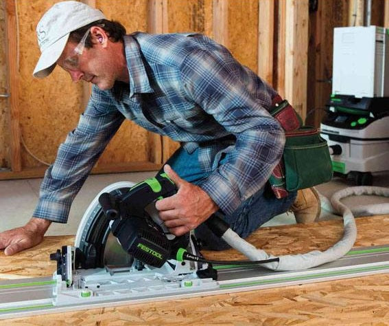 Man using green and black plungecut saw on wood panel with track guide in home improvement and power tools setting