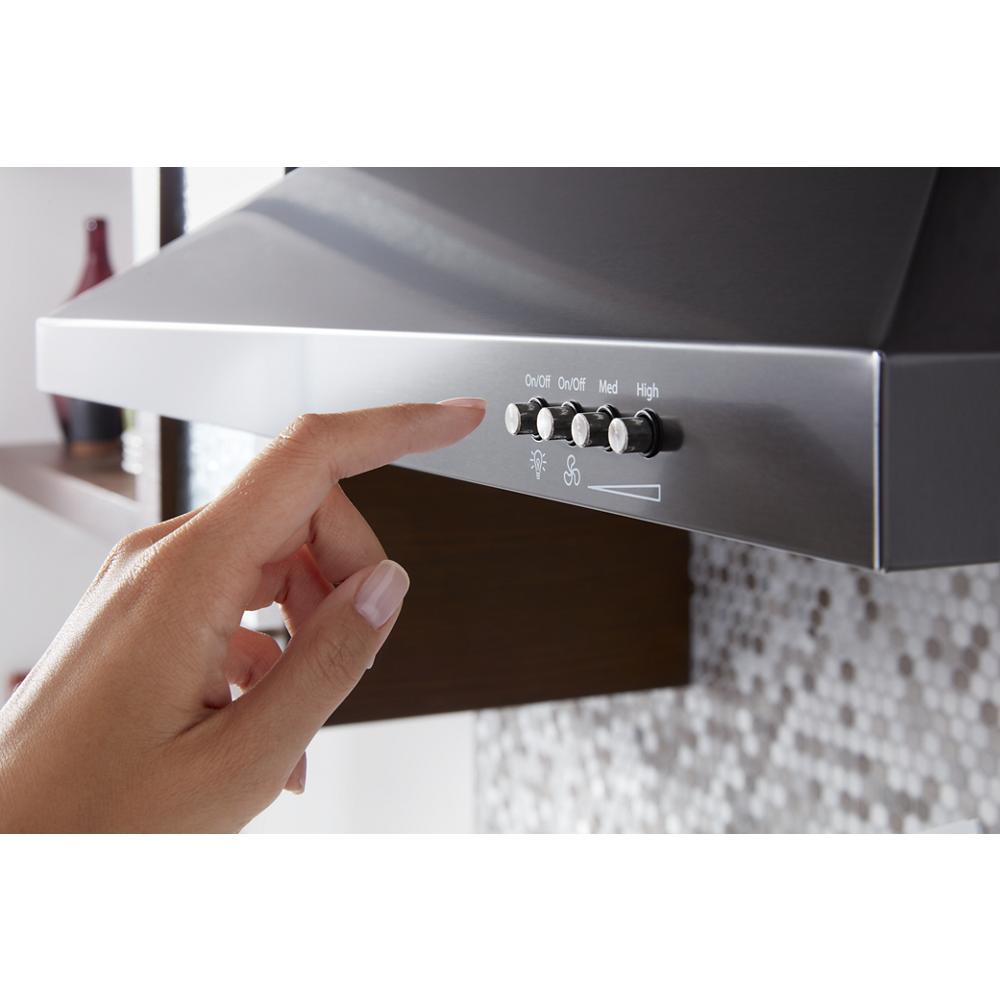 Close-up of hand adjusting control buttons on black stainless wall mount range hood in modern kitchen setting