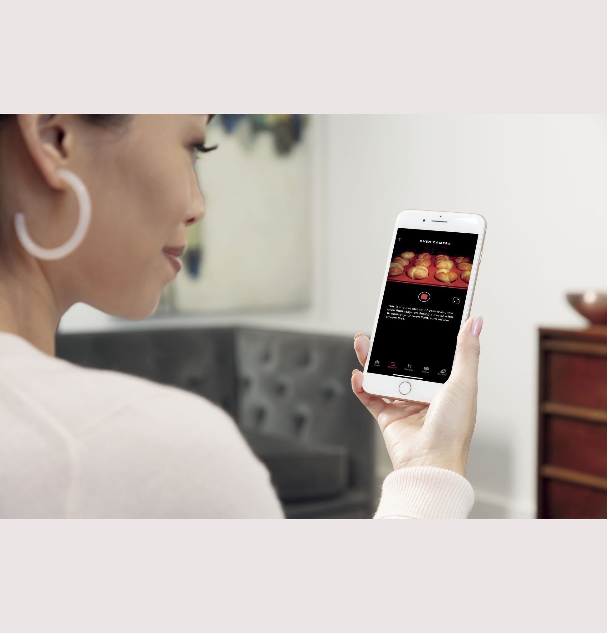 Woman viewing oven camera feed of baking food on smartphone in a modern kitchen and appliances setting