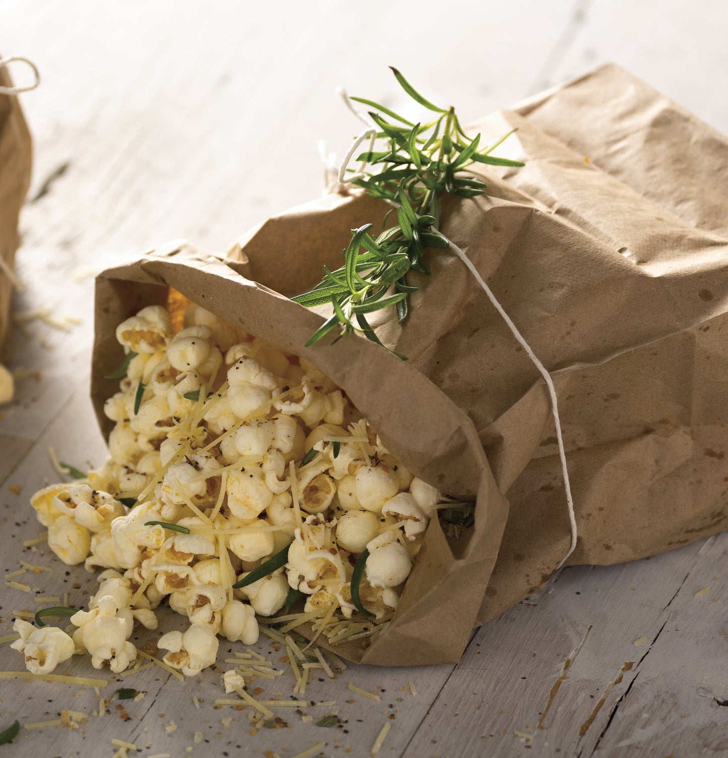 Popcorn seasoned with herbs and spices spilling out of a tied brown paper bag on a wooden surface