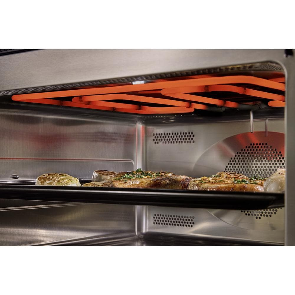 Interior view of stainless steel built-in microwave oven with orange heating element and cooked food on tray