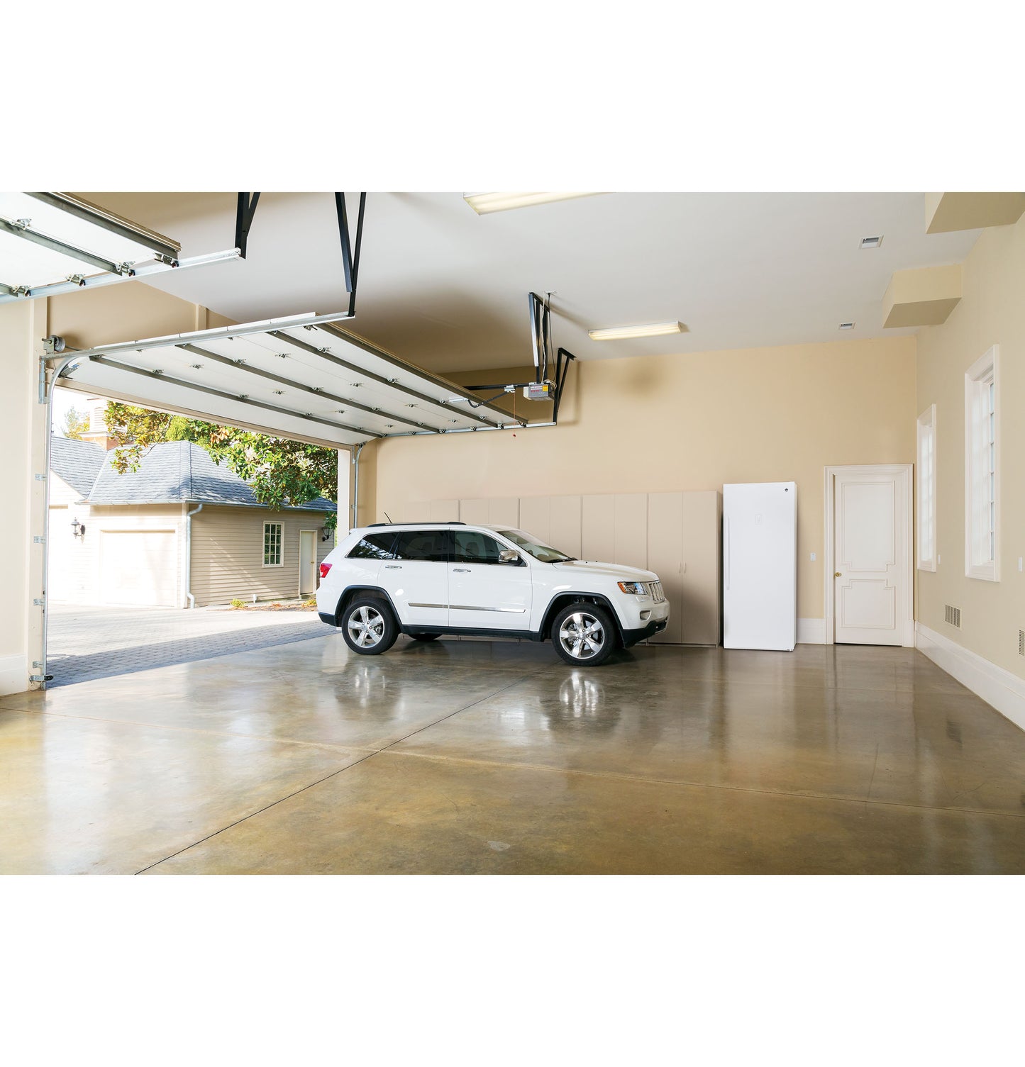 White upright freezer with closed door in spacious garage alongside parked white SUV in appliances collection