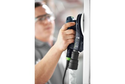 Person wearing safety glasses using Festool random orbit sander on vertical white surface for home improvement tasks