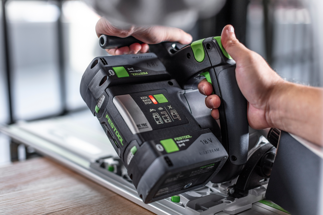 Hand holding Festool cordless track saw with guide rail cutting wood in workshop for home improvement tasks