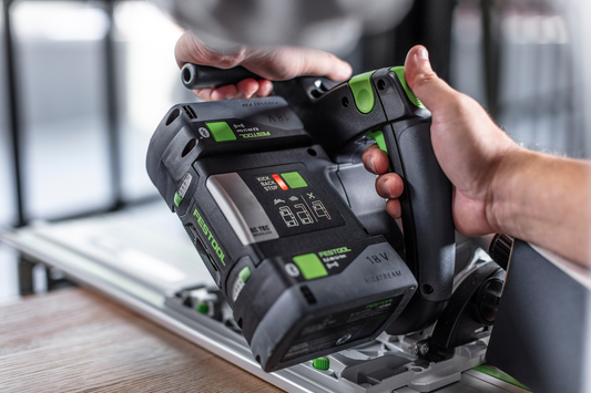 Hand holding Festool cordless track saw with guide rail cutting wood in workshop for home improvement tasks