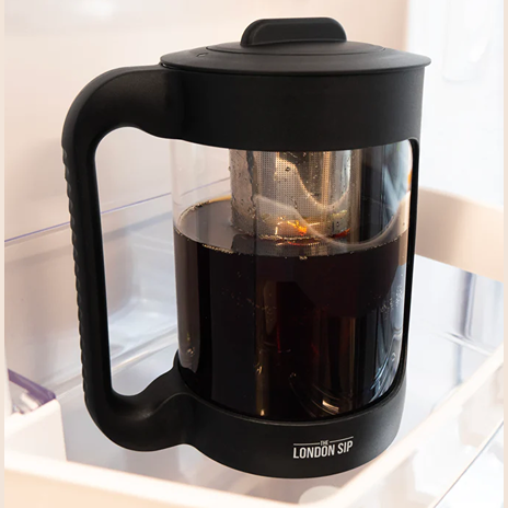 Clear glass cold brew maker with black handle and lid featuring stainless steel immersion filter in refrigerator door compartment