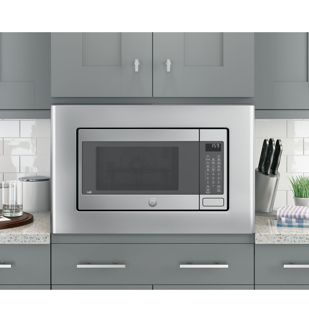 Built-in microwave with stainless steel optional trim kit installed in modern kitchen with gray cabinets and countertop accessories